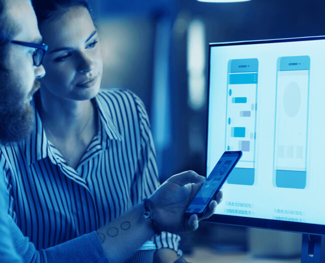 a man and a woman in front a computer discussing the development of an app